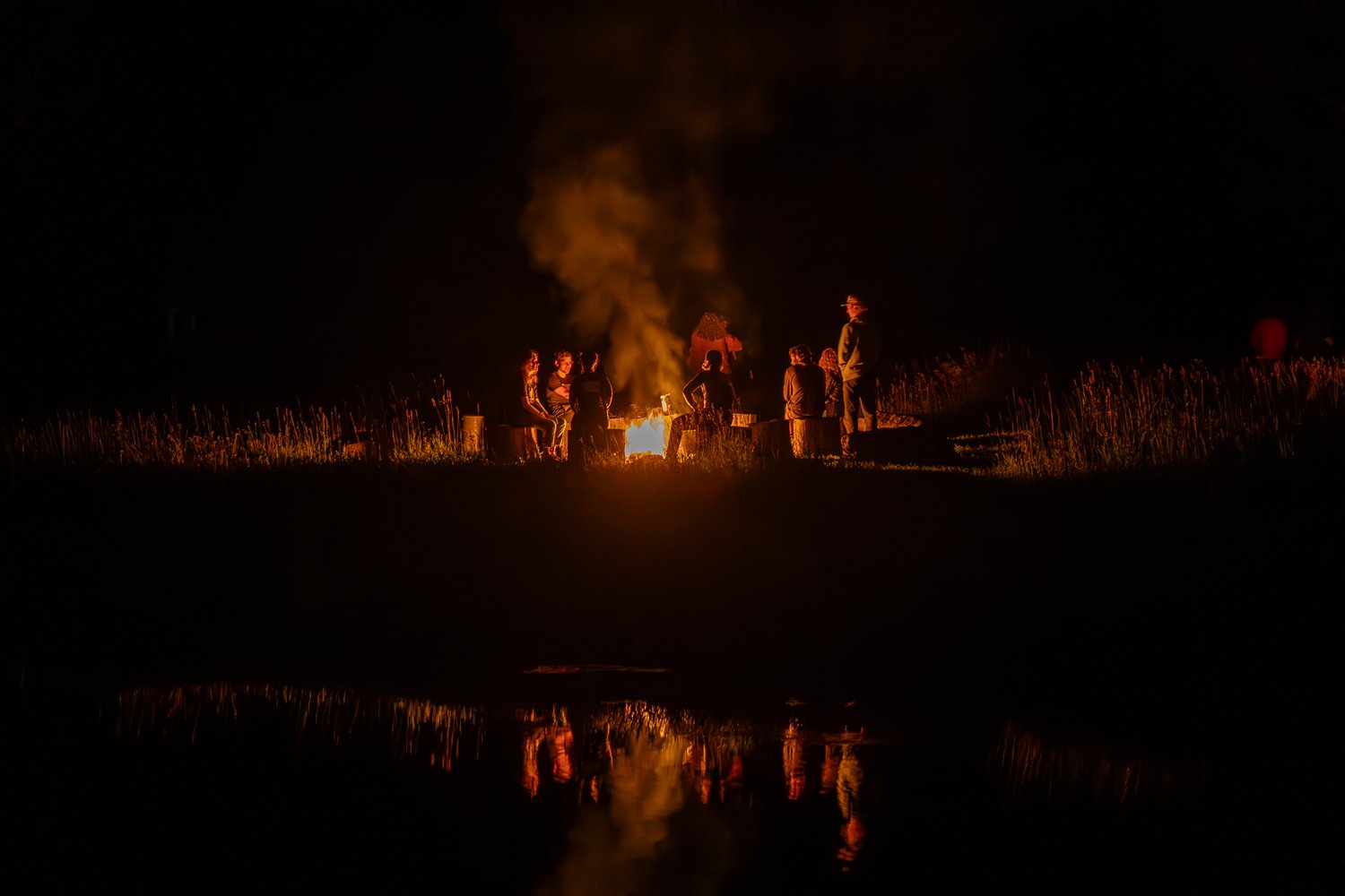 A group of people gathered around a fire in a field at night