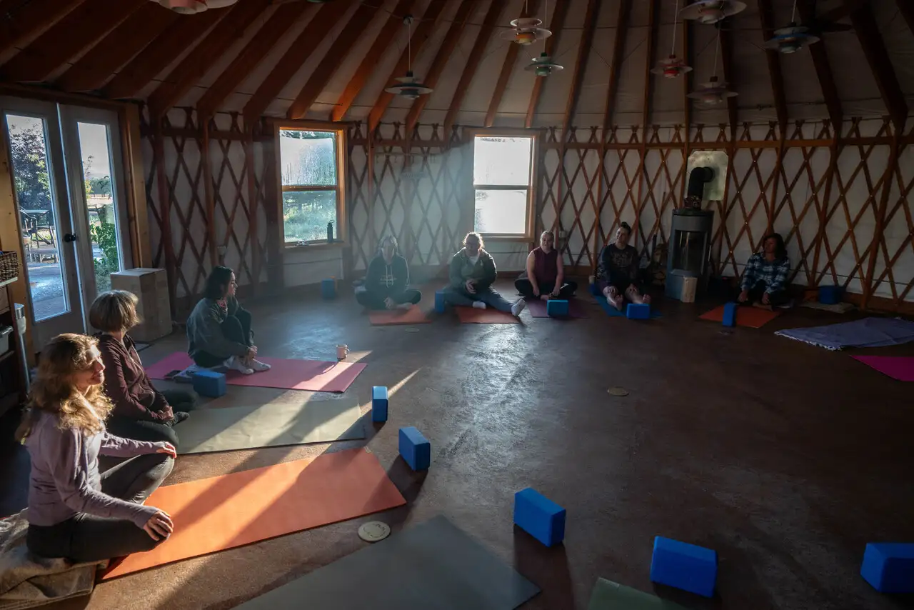 A group of people sitting on the floor in a circle, practicing yoga and meditation in a room with a round ceiling