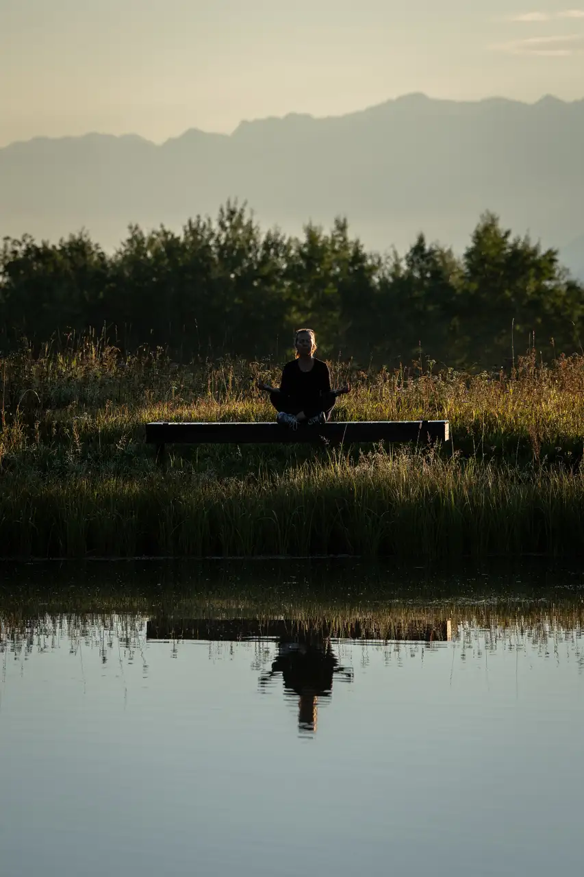 A woman meditating in a field near a pond