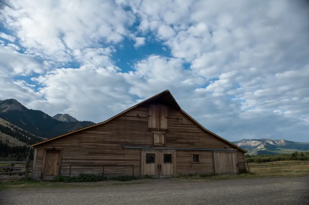 A barn with a sloped roof and a pointed top. The sky is cloudy and blue