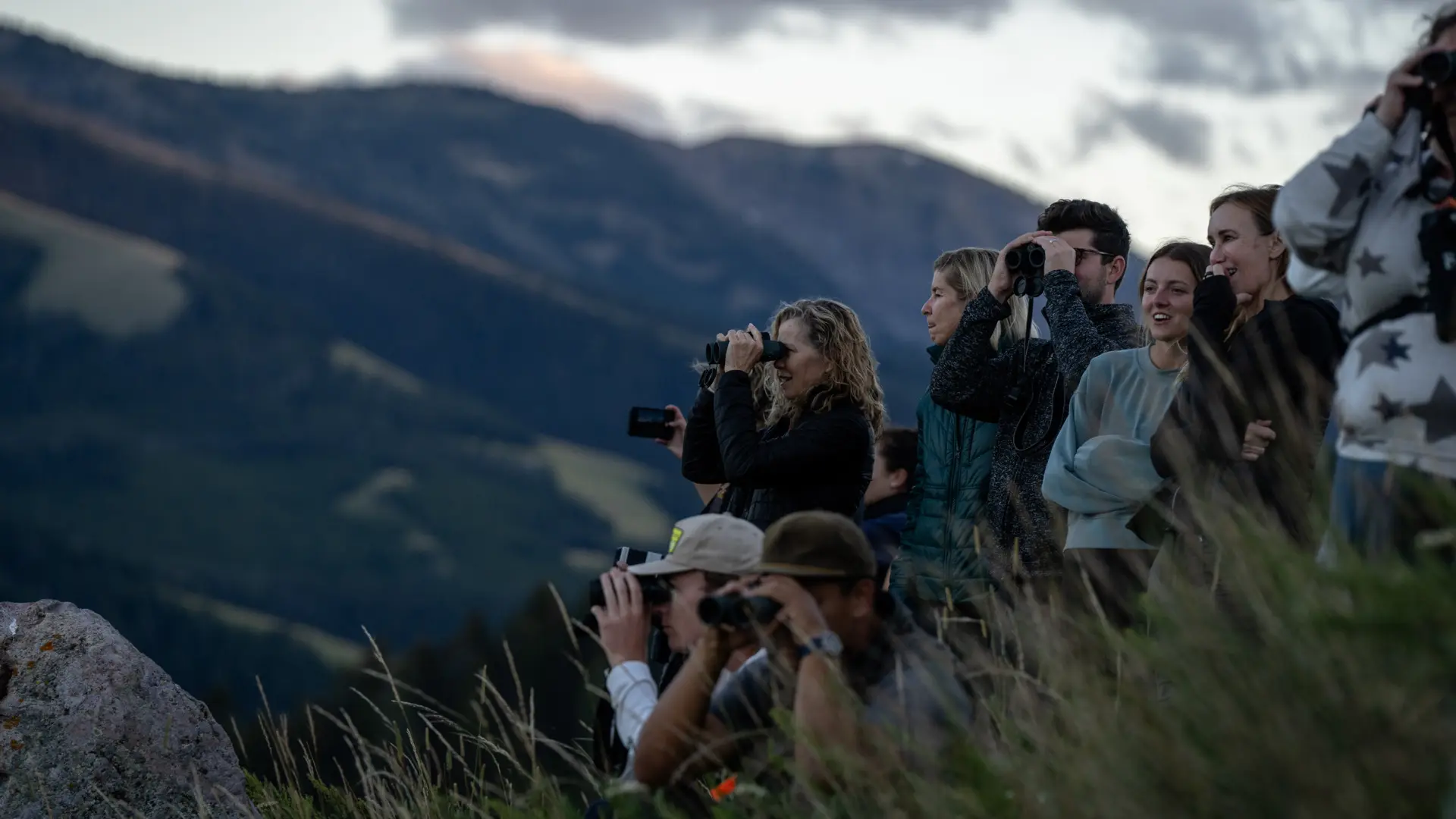 A group of people on a hill with cameras, looking at the mountains