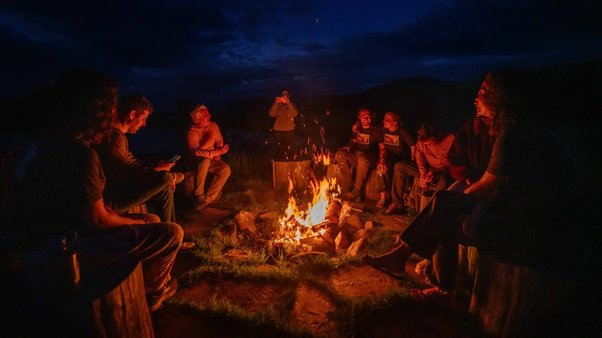 A group of people sitting around a fire pit, enjoying a camping trip together