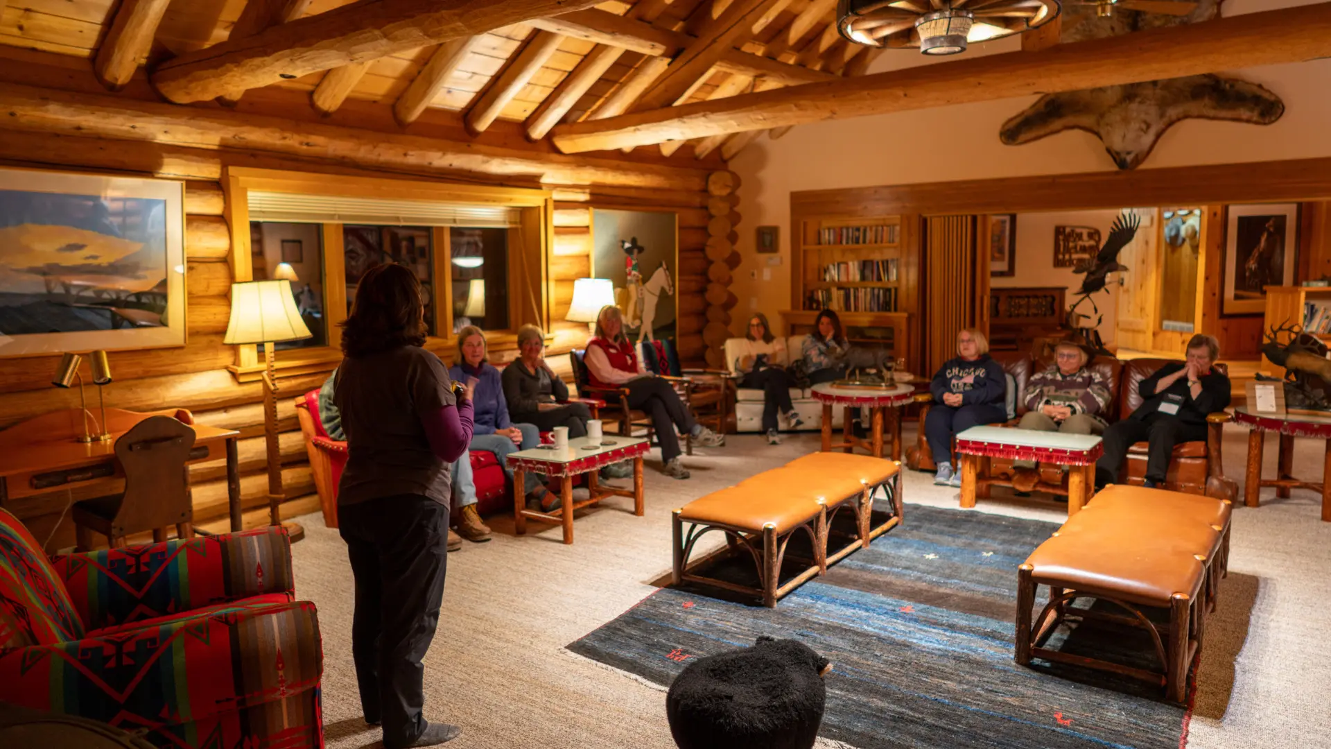 A group of people sitting in a living room with a woman standing in front of them