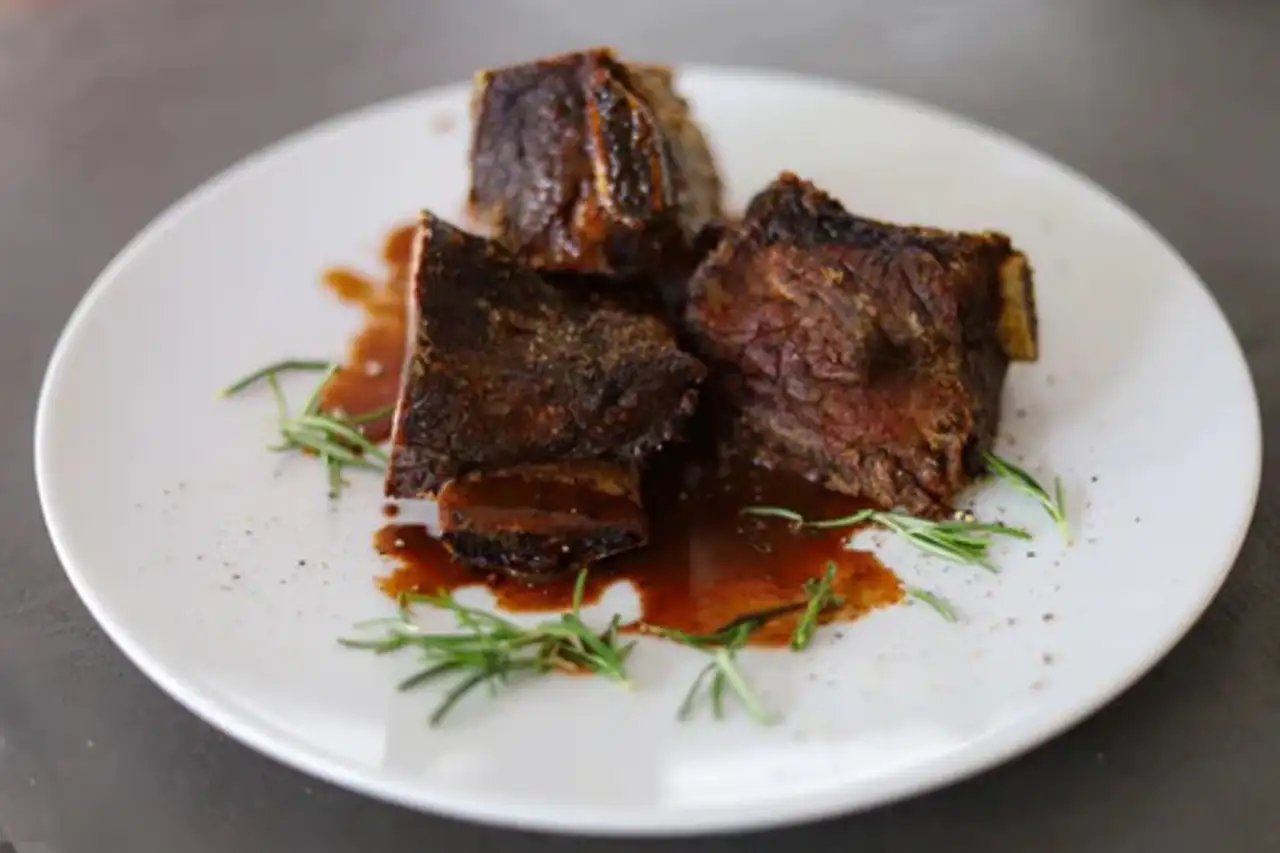 A piece of meat with a brown sauce and herbs on a white plate