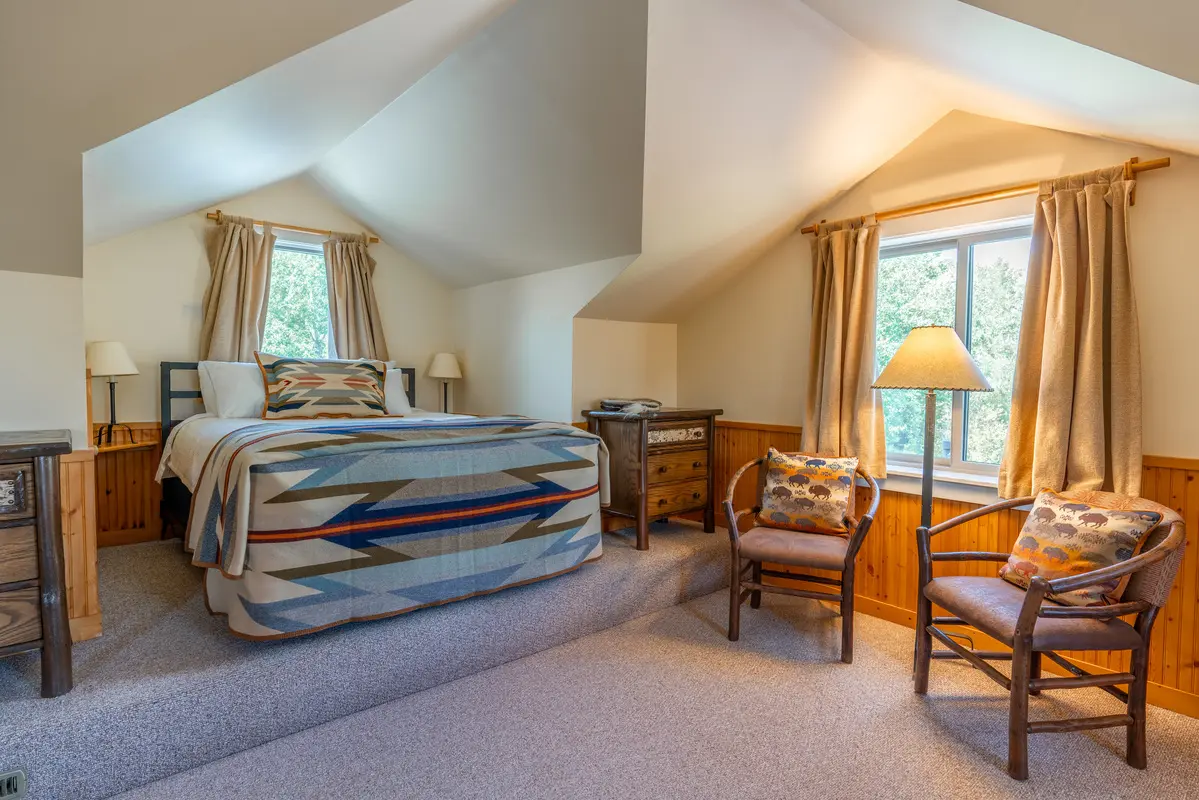 A bedroom with a striped blanket on the bed and a chair with a pillow on it