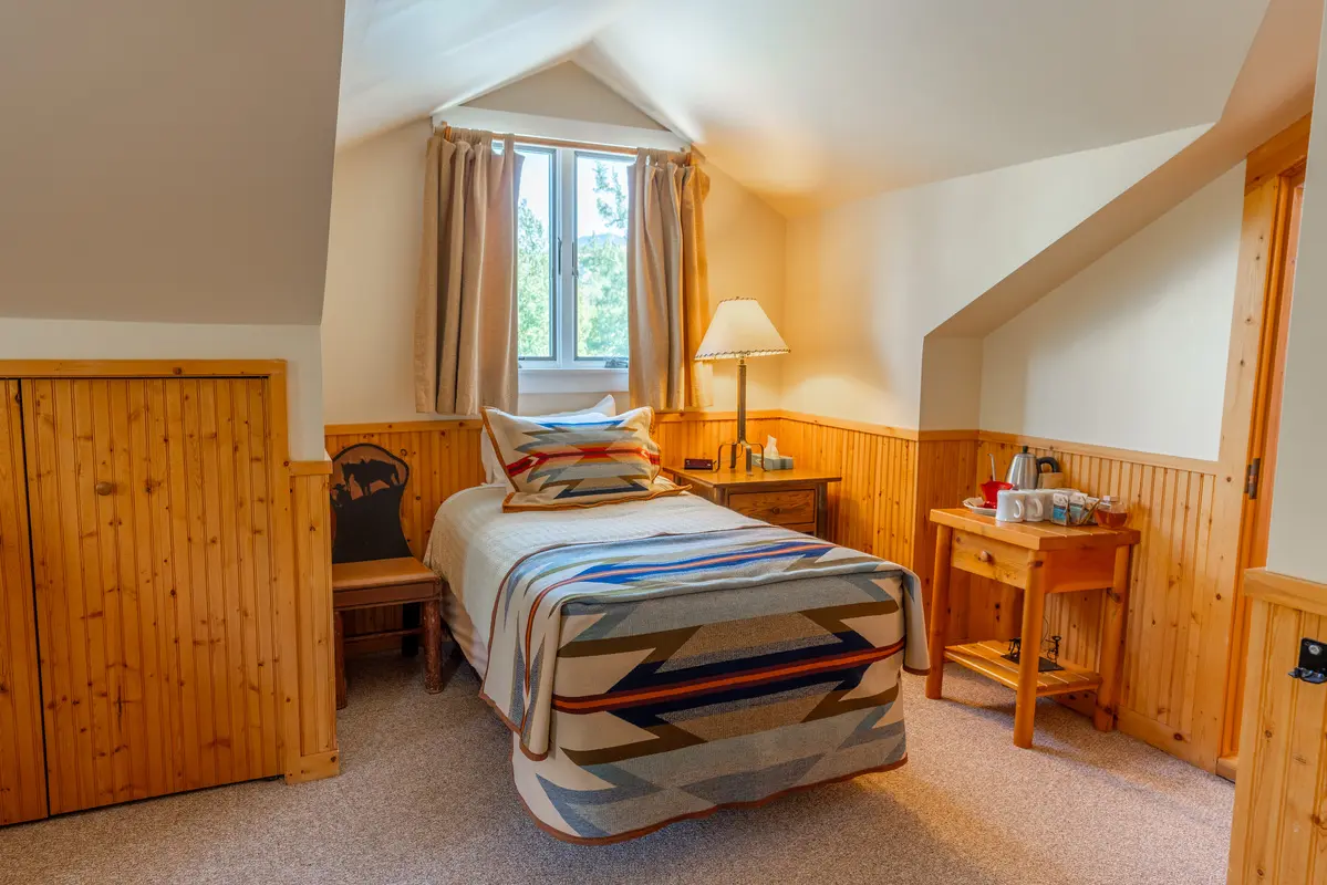 A bedroom with a bed and a nightstand. The bed has a southwestern blanket and a striped comforter. The room has a window and a lamp on the nightstand