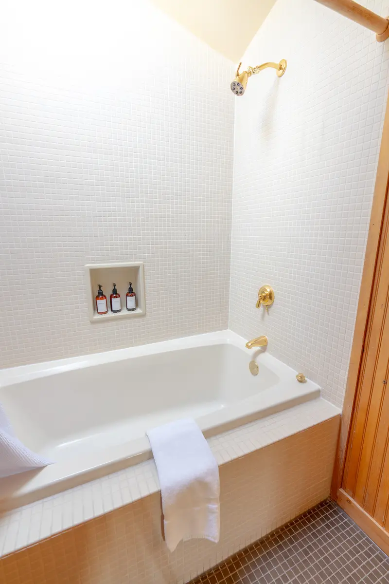 A white bathtub with a towel hanging on the side and a bottle of soap on the wall above it