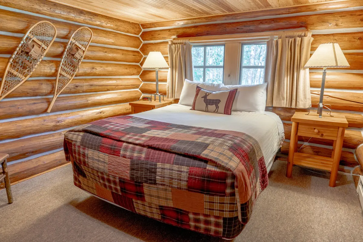 A bedroom with a bed and a window. The bed is covered with a plaid blanket and has a pillow with a deer on it