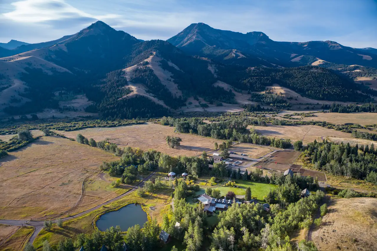 A valley with a house and lake in the foreground, surrounded by mountains and trees.