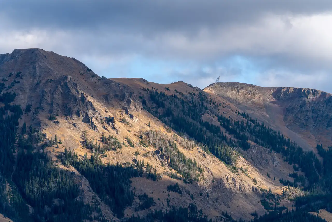 A mountain with a cloudy sky above it and a forest below it