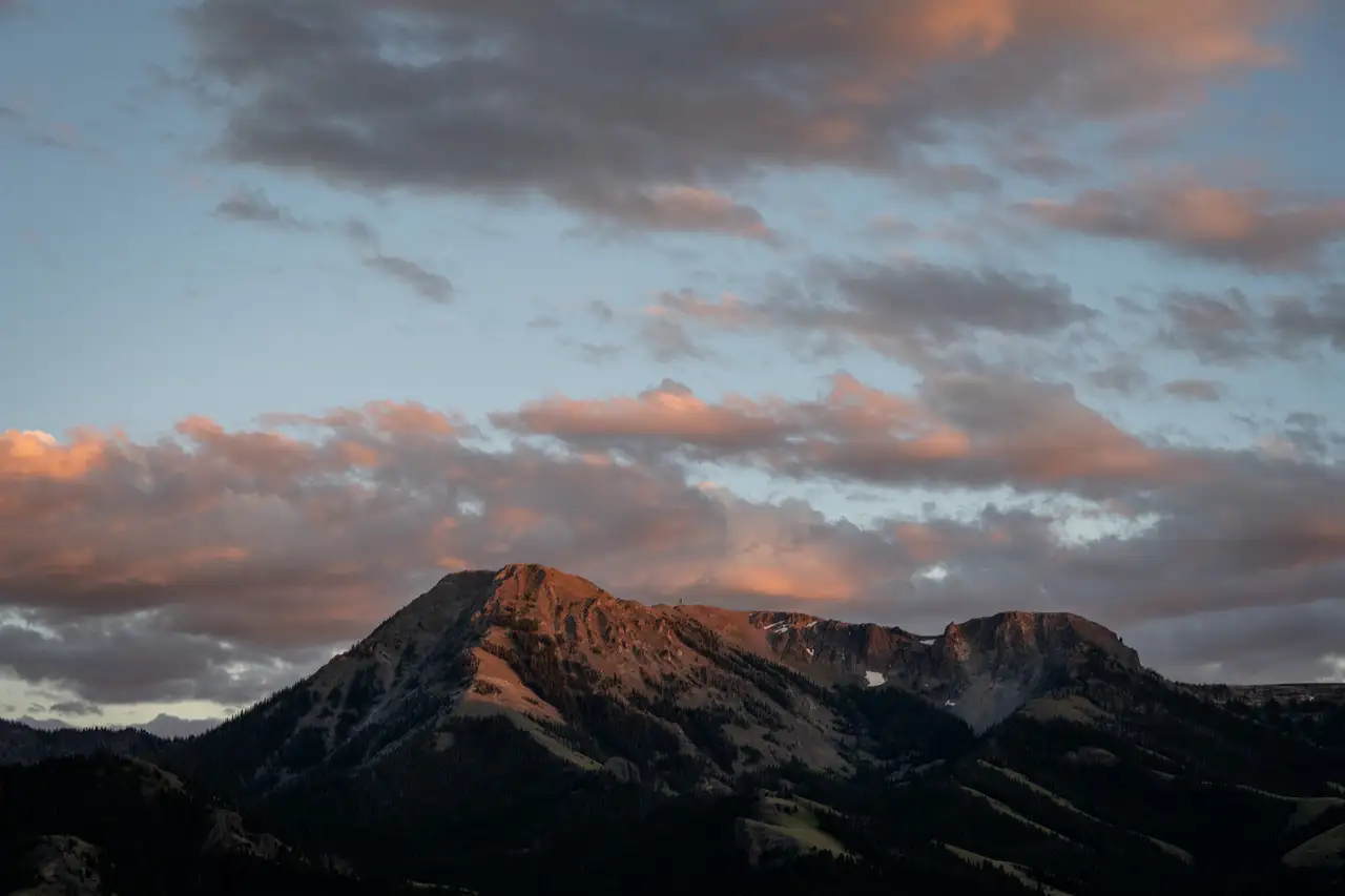 A mountain range with a cloudy sky and snowy peaks, set against a warm sunset