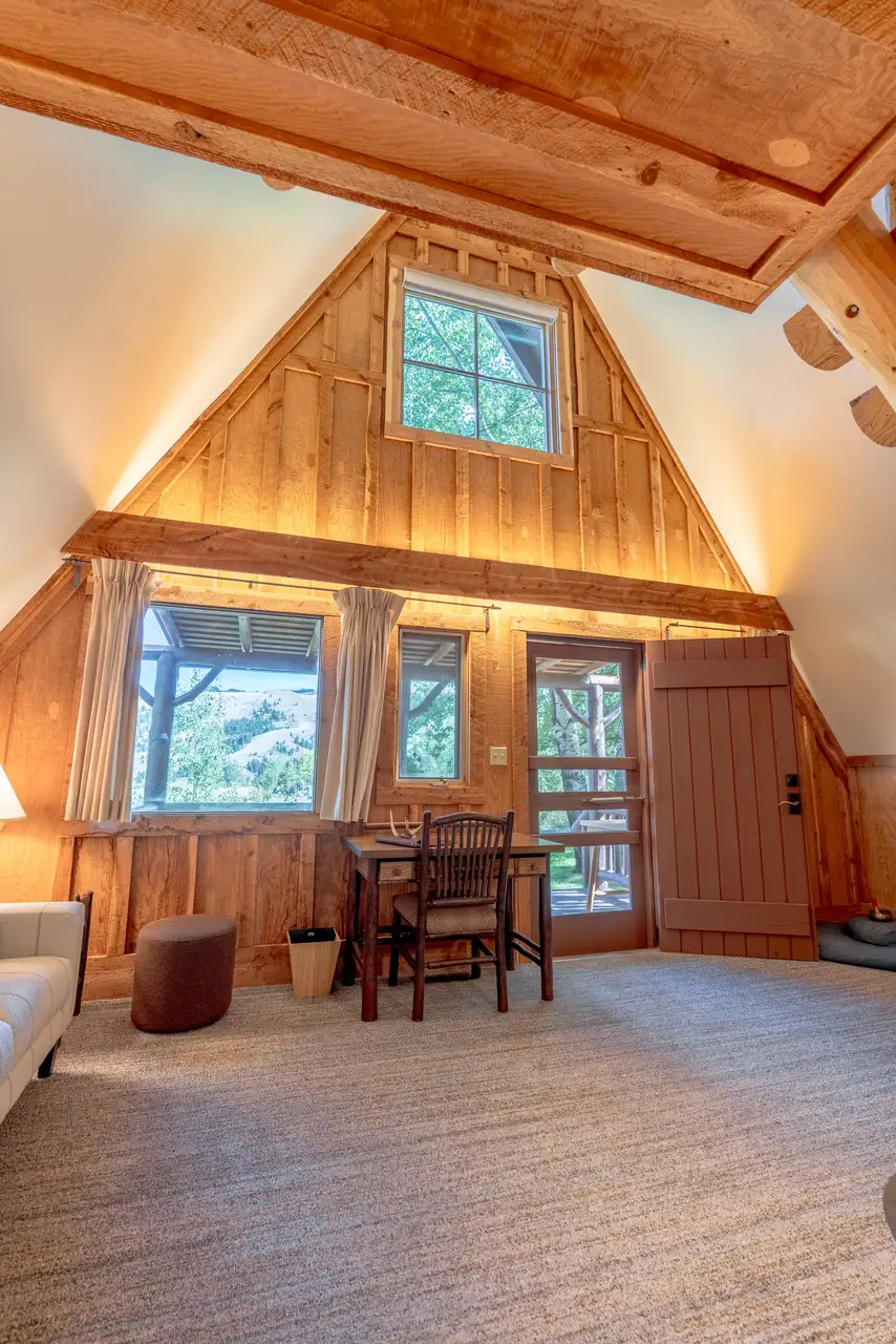 A living room with a wooden floor and ceiling, a couch, a chair, a table, a window, and a door