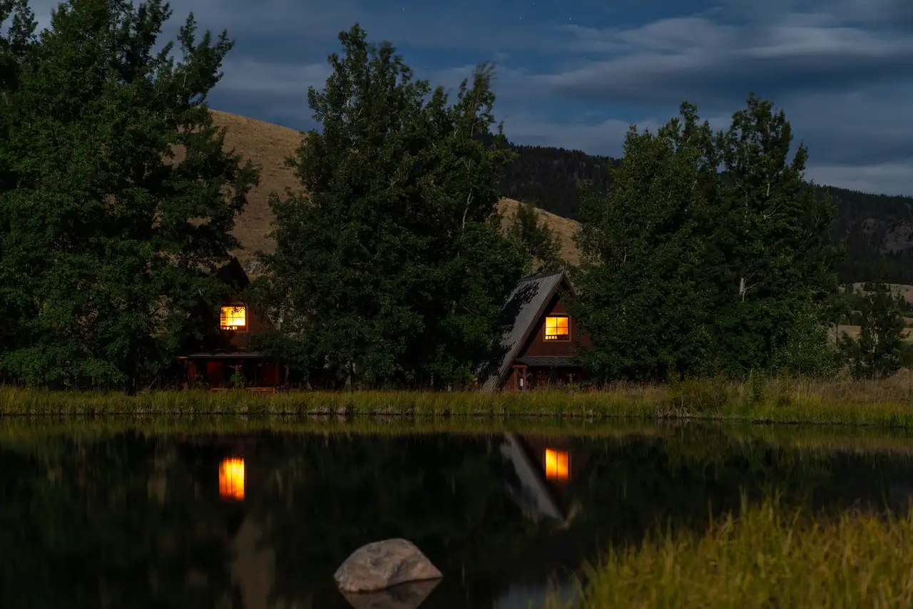 Two cabins on a hillside, surrounded by trees and water. The view is captured from the perspective of the water, creating a peaceful and picturesque atmosphere