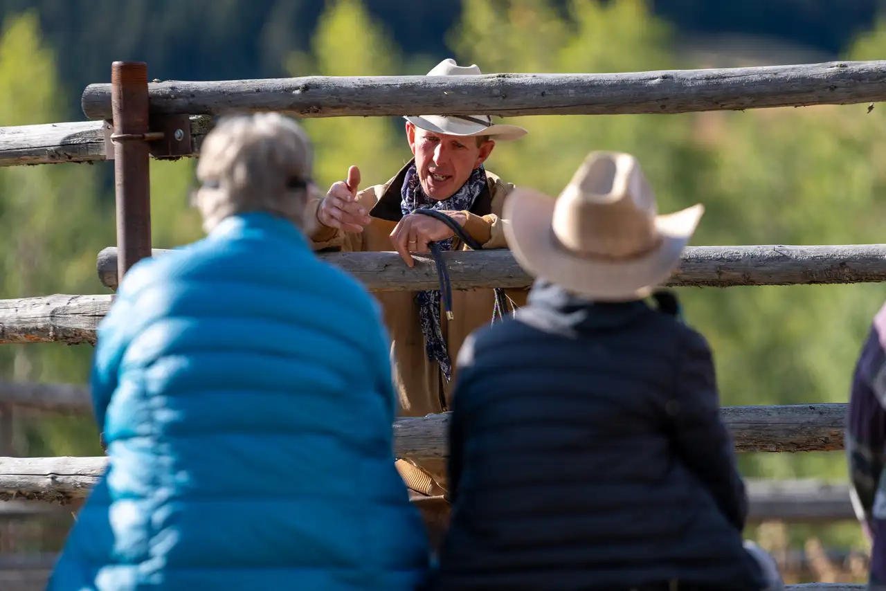 A man in a cowboy hat talking to two people behind a fence