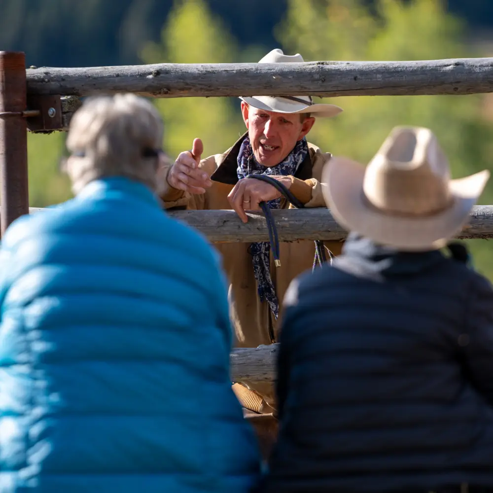 A man in a blue shirt and white hat talking to two women wearing cowboy hats