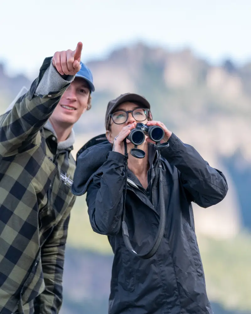 A man and woman looking through binoculars at something in the distance