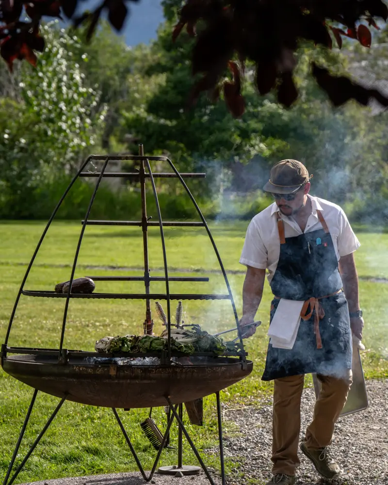 A man cooking food on a grill in a park-like setting