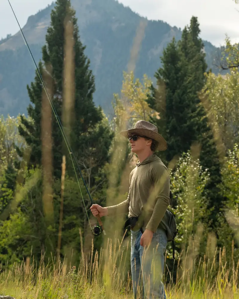 A man in a hat and sunglasses holding a fishing rod in a field with tall grass