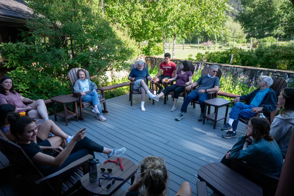 A group of people sitting on chairs and benches on a deck, enjoying each other's company and the outdoors