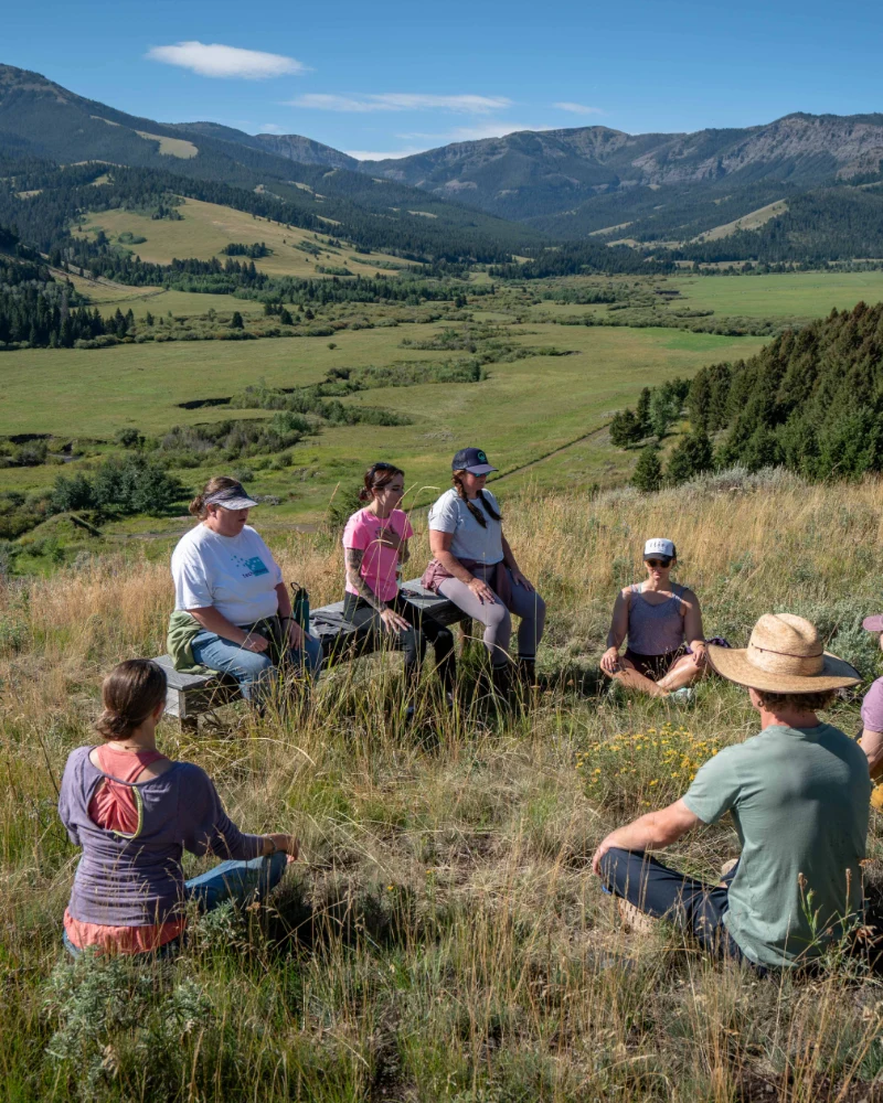 A group of people sitting on a hilltop, facing the same direction and enjoying each other's company