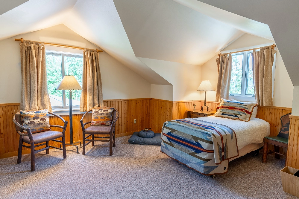 A bedroom with a bed, chair, and lamp. The bed is covered in a striped blanket and has a pillow on it