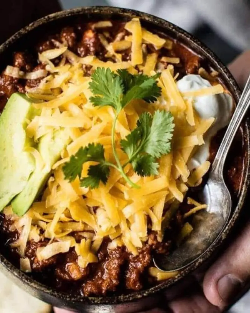 A bowl of chili with cheese and cilantro on top