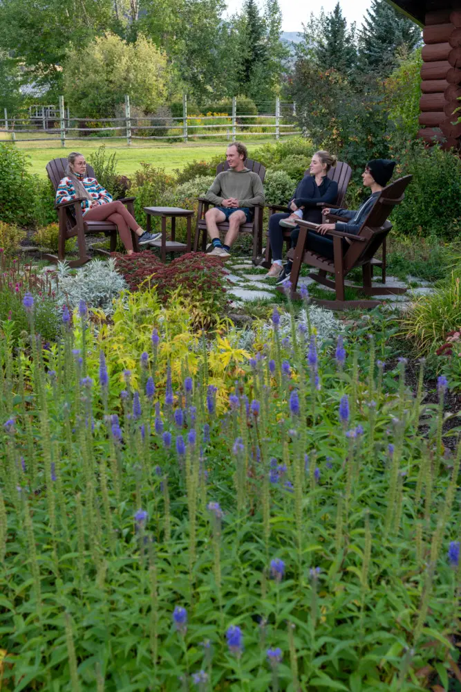 A group of people sitting in chairs in a garden, surrounded by flowers and plants