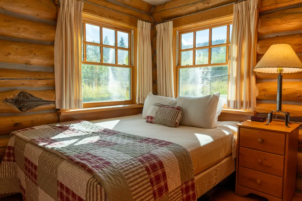 A bedroom with a bed and two windows. The windows are open