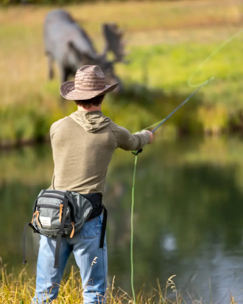 A man fishing in a river with a dinosaur statue in the background