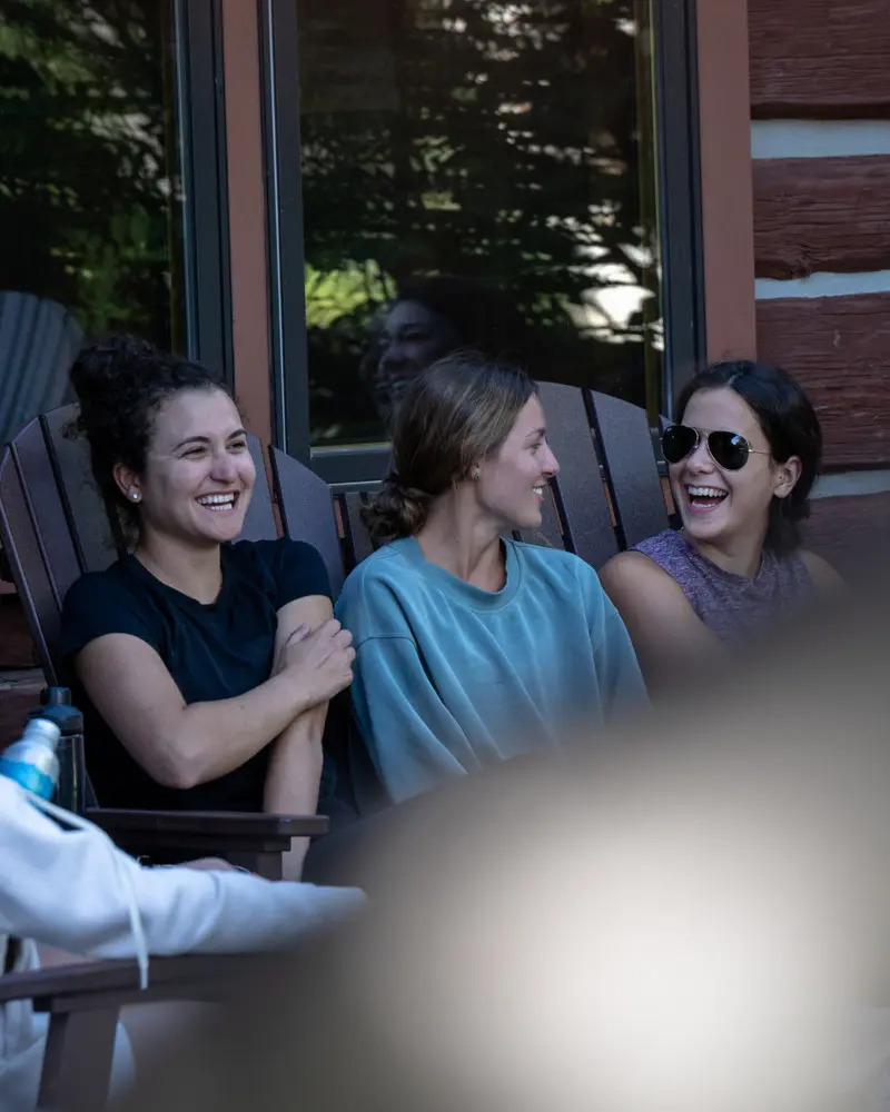 Three women sitting on chairs outside, laughing and smiling at each other