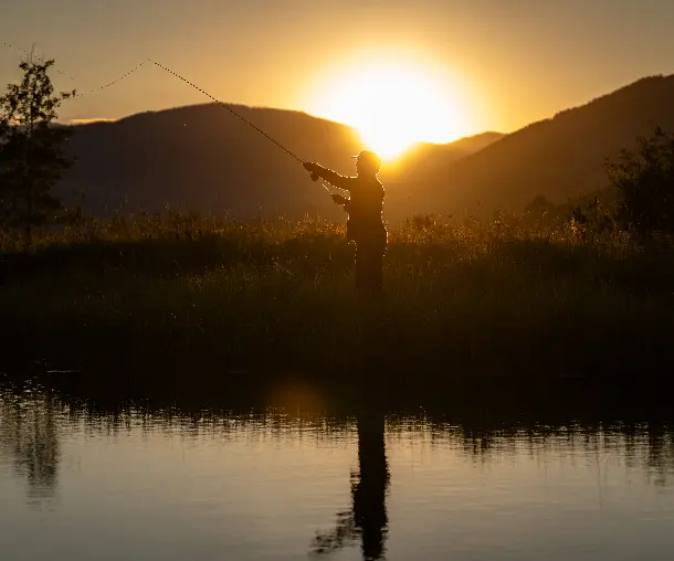 A person fishing in a lake at sunset