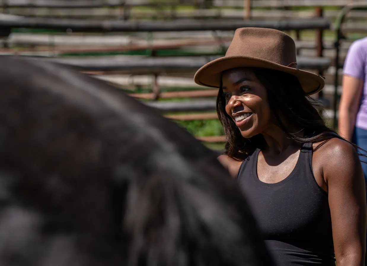 A woman wearing a brown hat is standing next to a horse