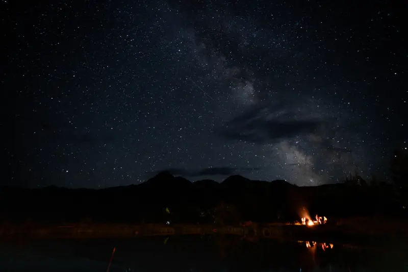 A nighttime scene with a sky full of stars, mountains, and a fire