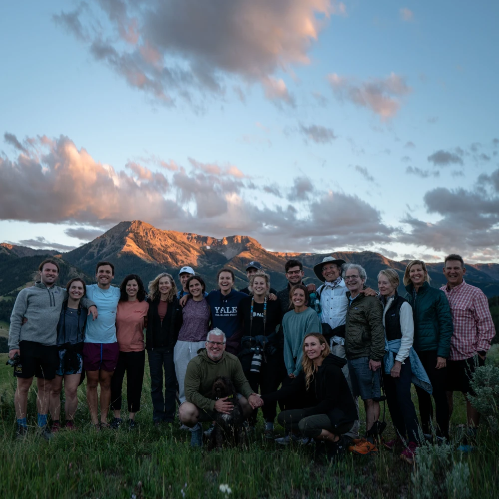 A group of people posing for a picture on a hill with mountains in the background