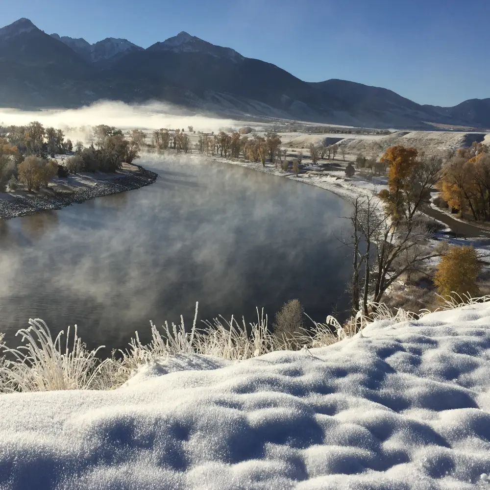 A snowy mountain landscape with a frozen lake and trees in the foreground