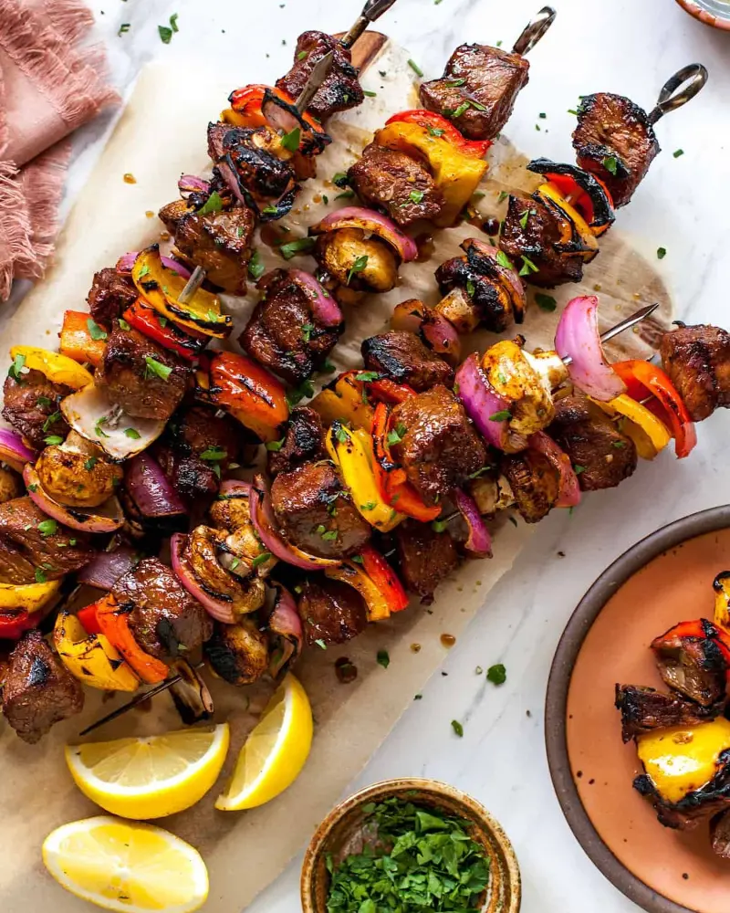 A wooden cutting board with a variety of shish kabob skewers and lemon wedges