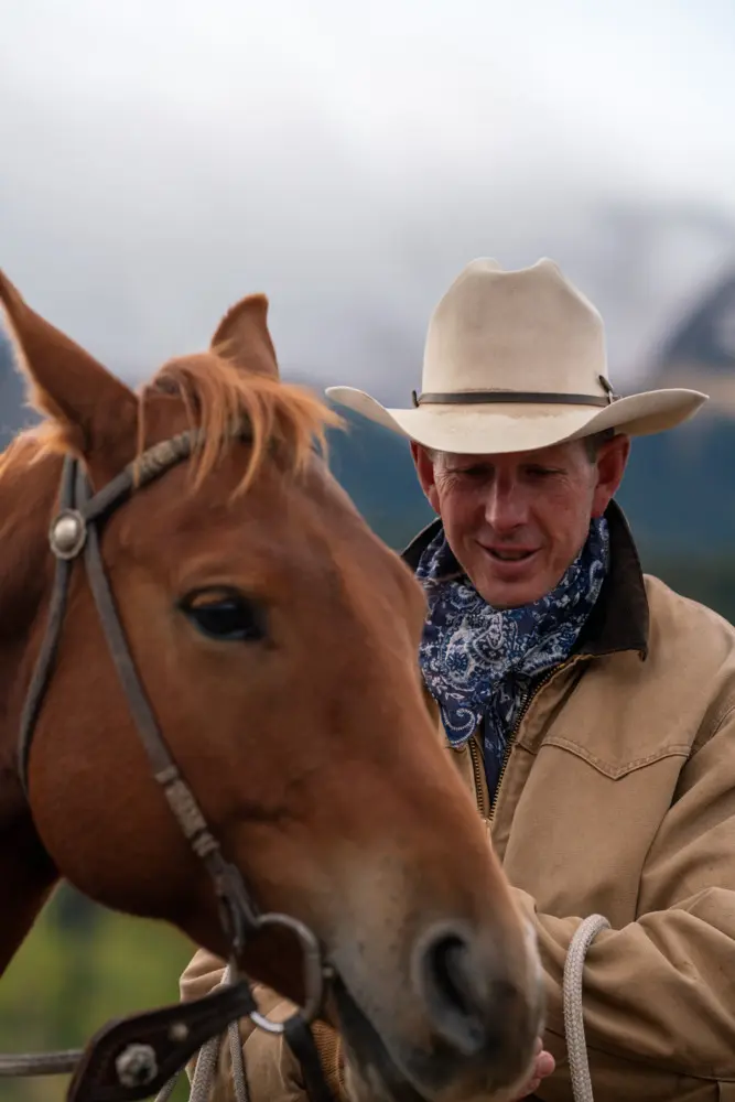 A man in a cowboy hat is petting a brown horse