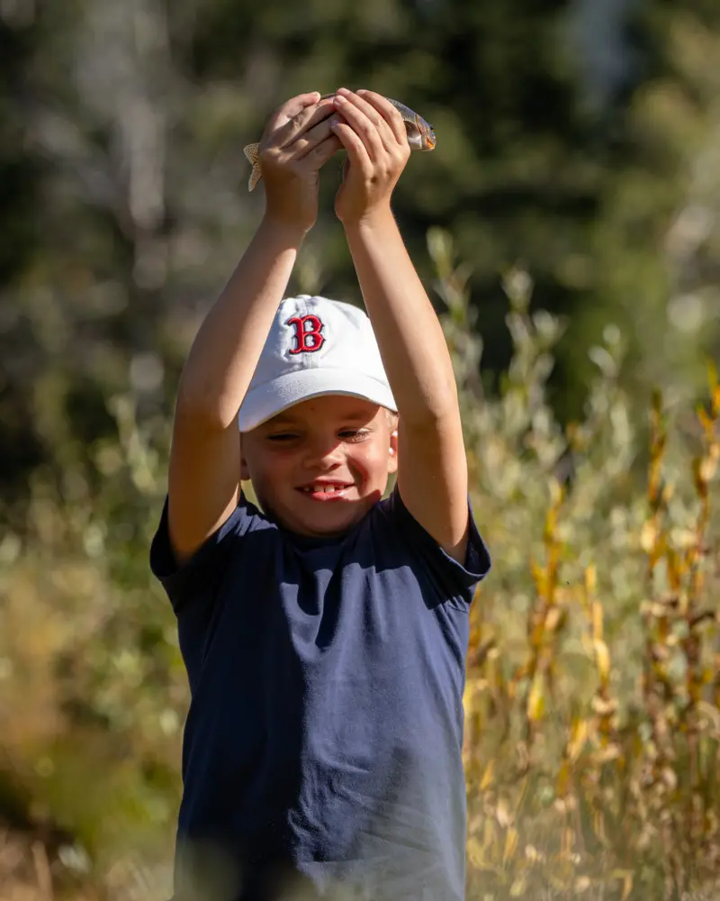 A young boy holding up a fish in a field