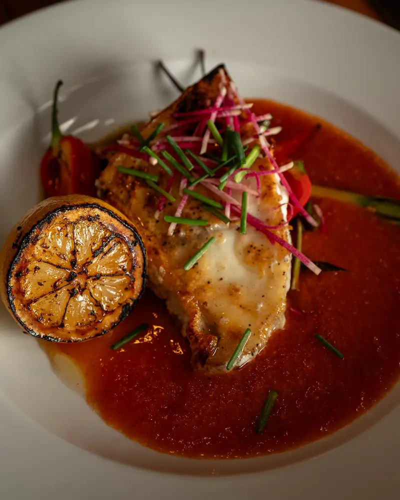 A plate of food with a red sauce, meat, vegetables, and a slice of lemon