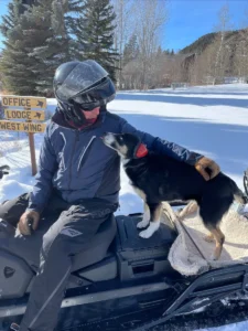 Mark and his dog sit on the snowmobile.